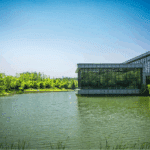 Bâtiment moderne près d'un lac et arbres verts.