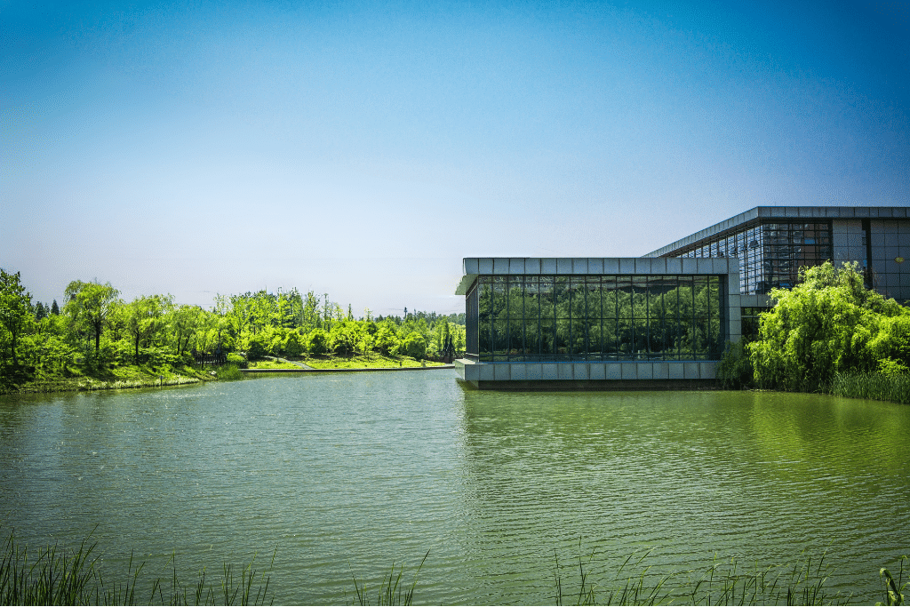 Bâtiment moderne près d&#039;un lac et arbres verts.