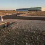 Terrain industriel viabilisé avec voirie neuve et halle moderne en arrière-plan